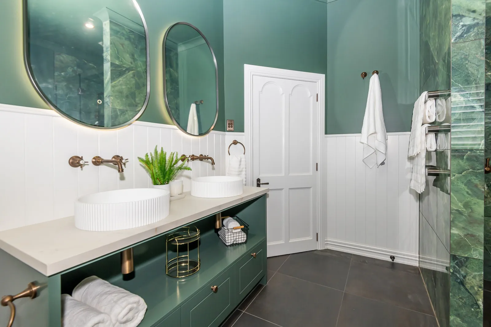 Image of newly renovated heritage bathroom in deep sage & white. Oval mirrors and round basins. Renovated by local Te Awamutu residential builders, Whitechurch Construction.